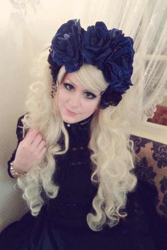 Meine Freundin im Gothic Lolita Look. Sie trägt eine wasserstoffblonde Lockenperücke mit riesigen dunkelblauen Rosen im Haar. Dazu ein schwarzes Kleid.