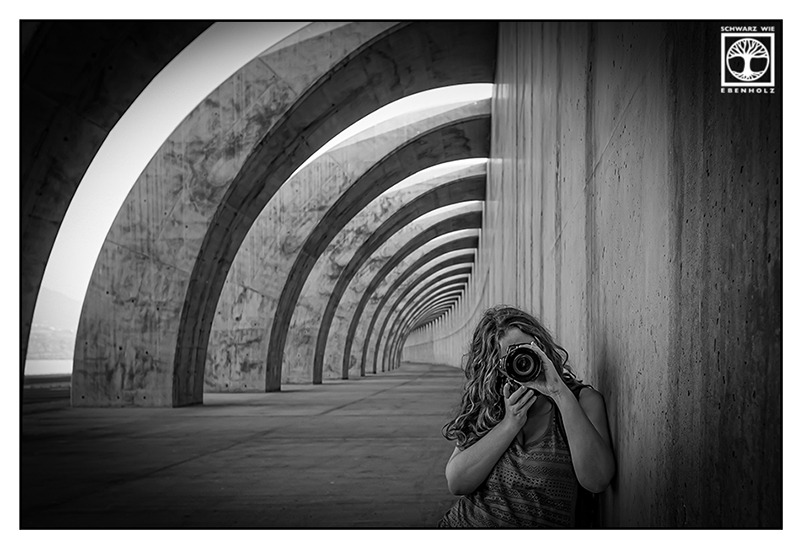 Melanie Hub steht in einem langen Tunnel mit gebogenen Säulen und richtet die Kamera direkt auf Dich!