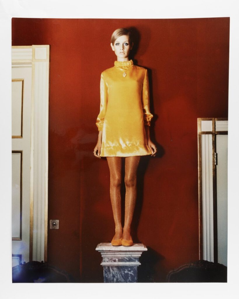 Dieses Bild von Twiggy im gelben Minikleid vor einer roten Wand auf einem Marmorpodest ist gemeinfrei. Es wurde 1967 von Cecil Beaton in London aufgenommen. Quelle: https://collection.sciencemuseumgroup.org.uk/objects/co8642537/twiggy-photograph